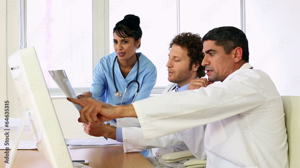 Doctors sitting at desk talking about xray with a nurse Doctors sitting at desk talking about xray with a nurse