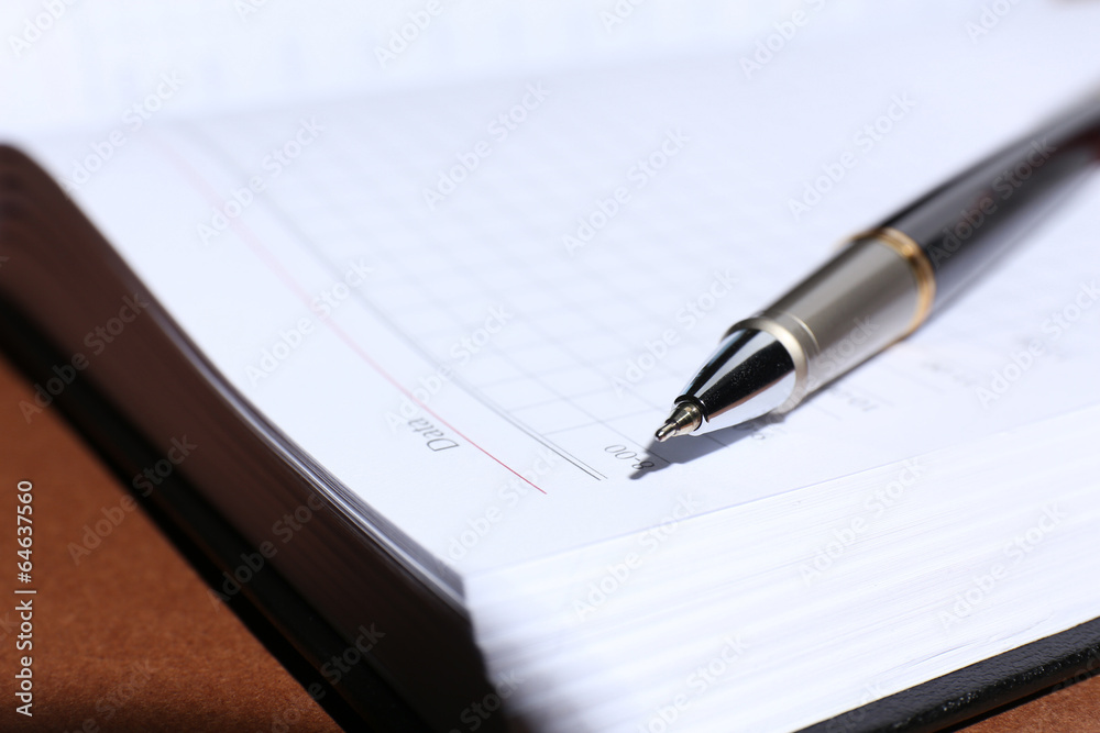 Pen on opened book on brown table Pen on opened book on brown table