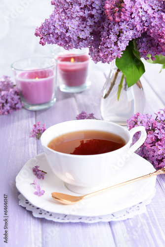 Beautiful lilac flowers with cup of tea on table close-up