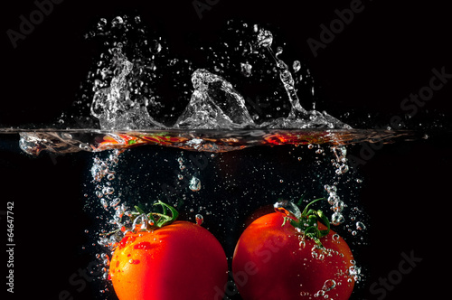 Two tomatoes falling into water before black background