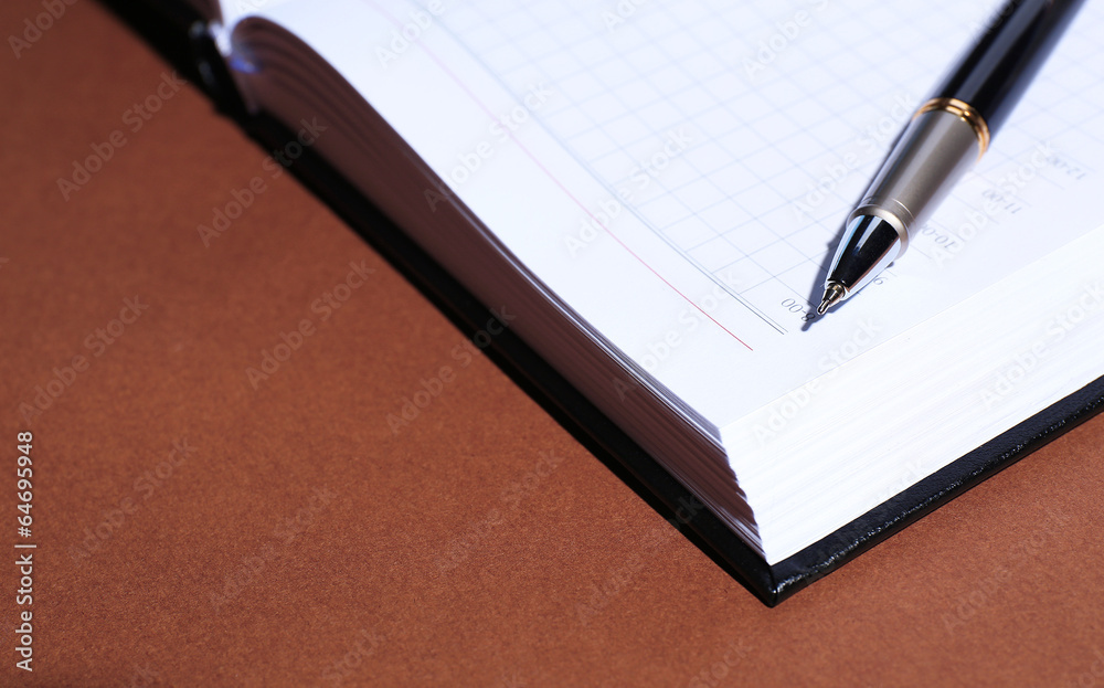 Pen on opened book on brown table Pen on opened book on brown table