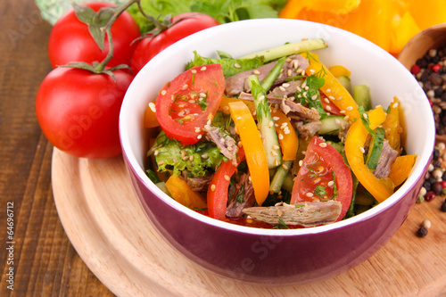 Beef salad in bowl with vegetables and spices on wooden table