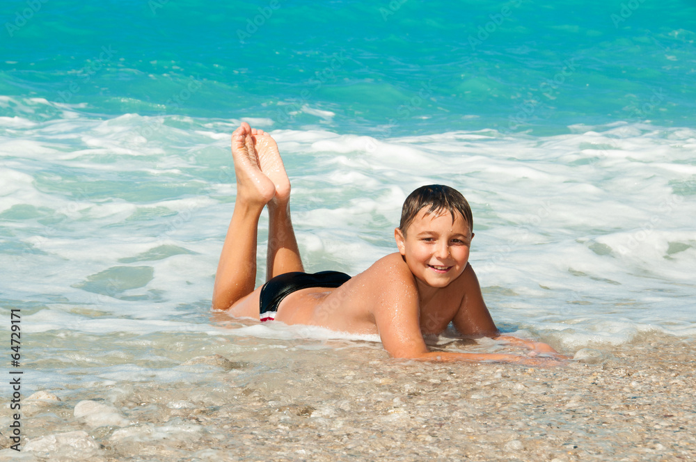 Fototapeta premium Boy at the sea lying on the sand and waves