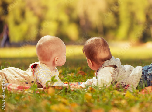 two baby boys looking away laying on a carpet at park grass