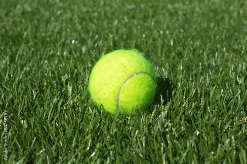 Yellow tennis ball lays on synthetic grass court closeup © DyMaxFoto