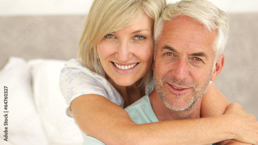 Couple embracing and smiling at camera in bed together Couple embracing and smiling at camera in bed together