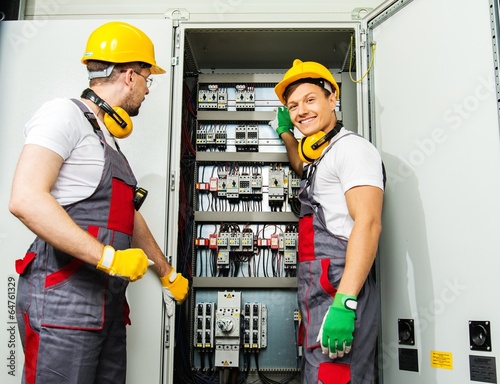 Two electricians in a safety hat and headphones on a factory