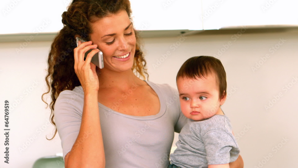 Mother holding her baby son in the kitchen talking on phone Mother holding her baby son in the kitchen talking on phone