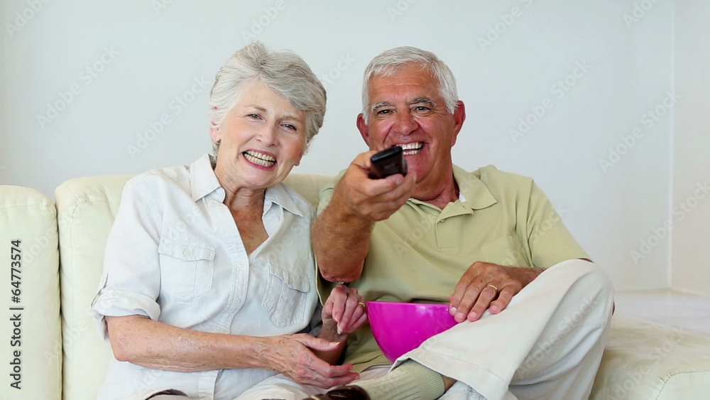 Senior couple sitting on sofa watching tv Senior couple sitting on sofa watching tv