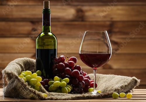 Fototapeta Naklejka Na Ścianę i Meble -  Bottle of red wine, glass and grape on a sack in wooden interior