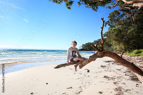 Cheerful teen boy sitting on tree  holiday at the beach Australi photo
