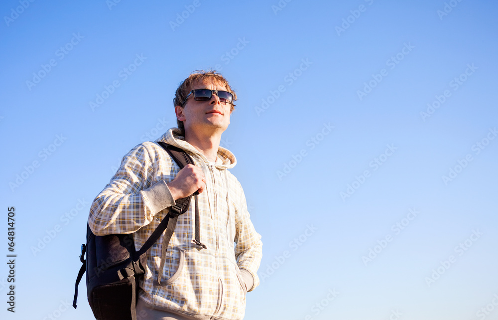 Happy man hiker holding backpack on a blue sky