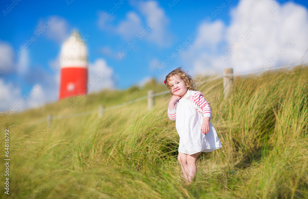 Adorable toddler girl next  red lightshouse on a beach