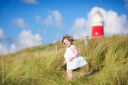 Cute toddler girl next to red lightshouse on a beach photo