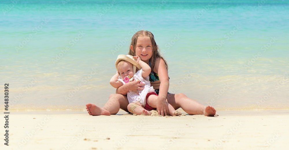 Two happy smiling sisters sitting on a tropical beach.
