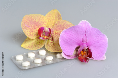 Two orchid flowers with film-coated tablets on gray