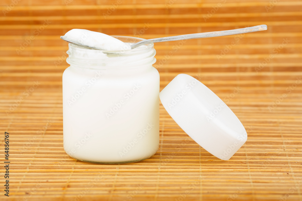 the jar with yoghurt and spoon on a straw mat the jar with yoghurt and spoon on a straw mat