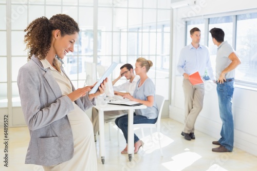 Pregnant businesswoman using tablet with team behind her