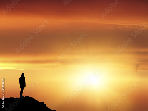 Man silhouette on top of a mountain looking the horizon concept of success 