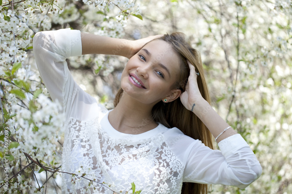 Beautiful young girl standing near blooming trees in spring gard