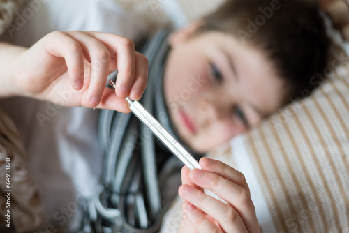Sick boy with thermometer lying in bed photo