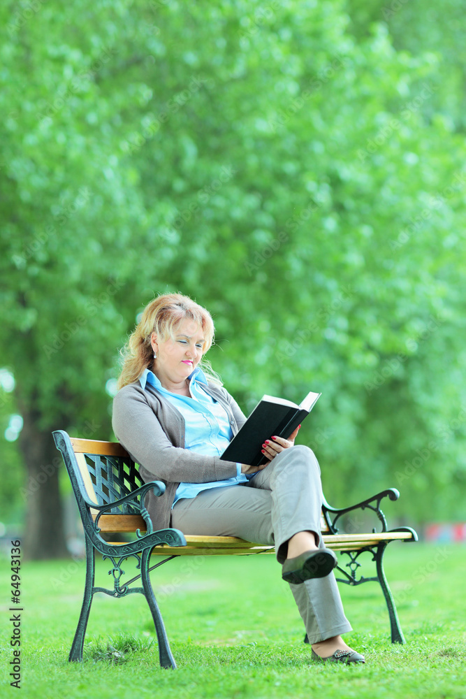Mature lady reading a novel seated on a bench