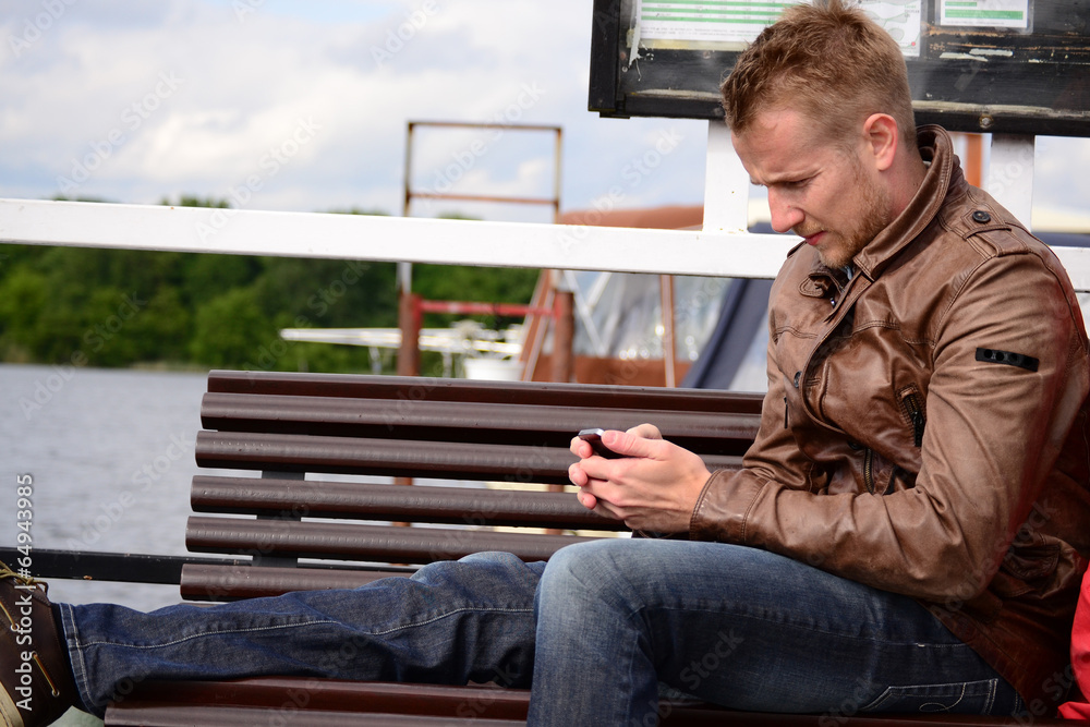 young blond man sitting on a bench and looking at smartphone