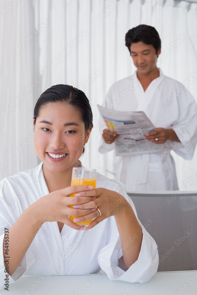 Woman in bathrobe having orange juice with boyfriend in backgrou Woman in bathrobe having orange juice with boyfriend in backgrou
