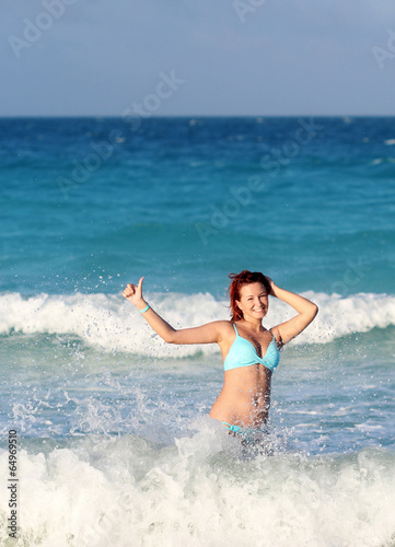 Smiling young redhead woman standing in the ocean wave