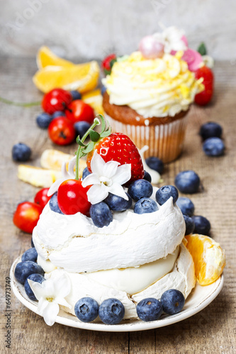 Meringue cake decorated with fresh fruits, standing on wood