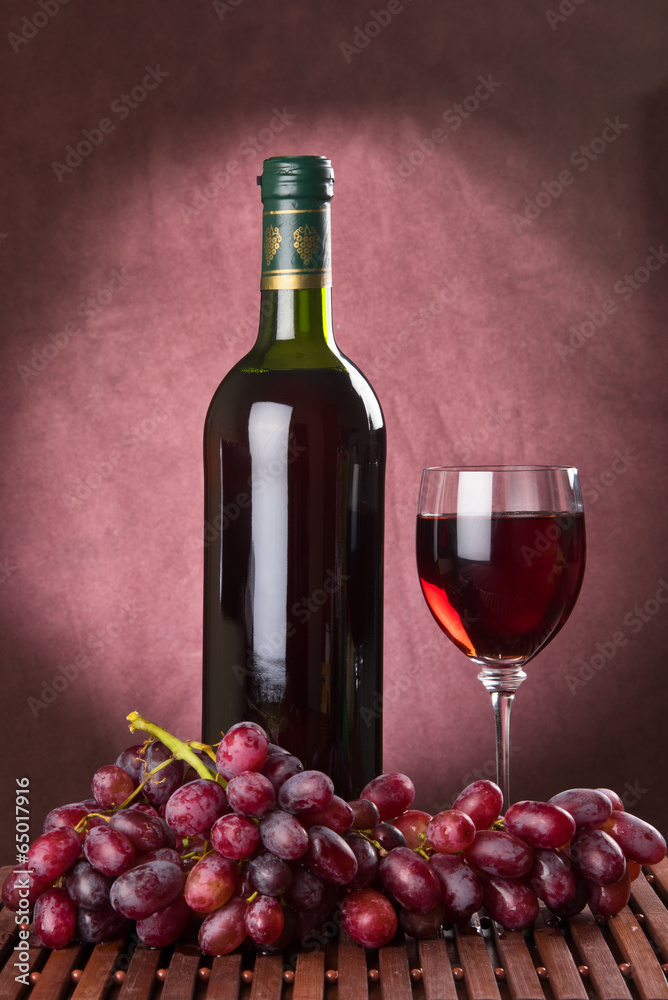 Bottle and wine glass with red wine and red grapes
