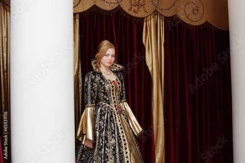 Actress in royal dress posing on curtain backdrop