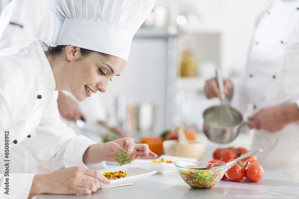 closeup on a female chef preparing a dish her team in the backg closeup on a female chef preparing a dish her team in the backg