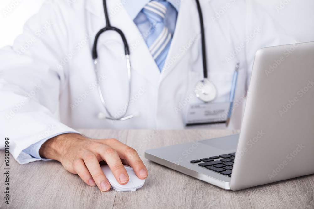 Midsection Of Doctor Using Laptop And Mouse At Desk