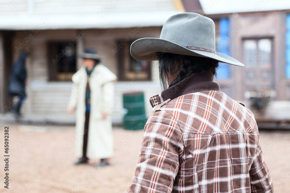 Cowboy with hat standing against another man in street
