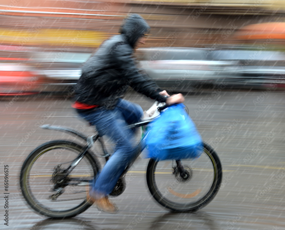 Fototapeta premium Cyclist in motion riding down the street on rainy day