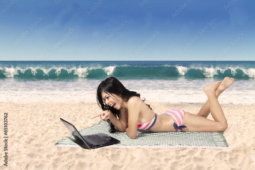 Happy woman in bikini with laptop at beach