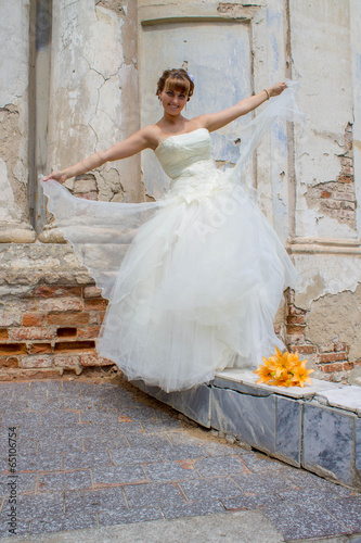Невеста идет по бордюру, букет желтых лилий у старой церкви