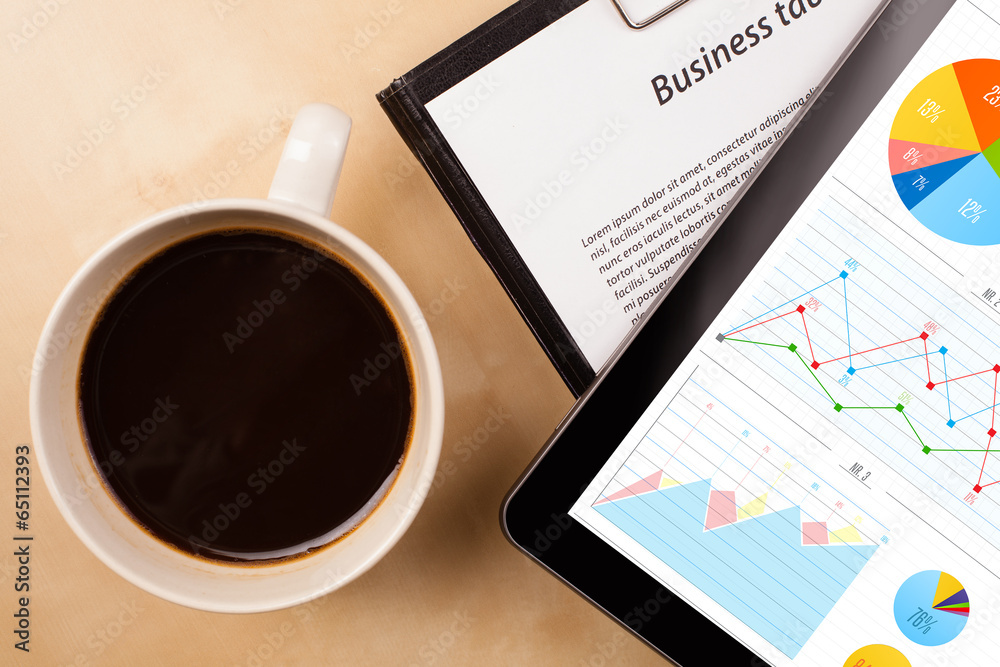Tablet pc shows charts on screen with a cup of coffee on a desk Tablet pc shows charts on screen with a cup of coffee on a desk