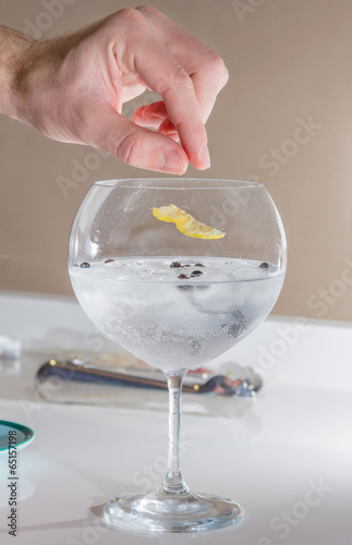 Barman putting lemon peel to prepare gin tonic