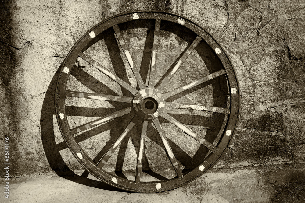 An old wagon wheel,leans against a stucco wall.