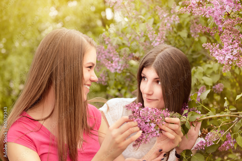 Two young women walking outside in a park at the lilac tree Two young women walking outside in a park at the lilac tree