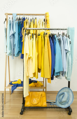 Color coordinated yellow and blue clothes on hangers.