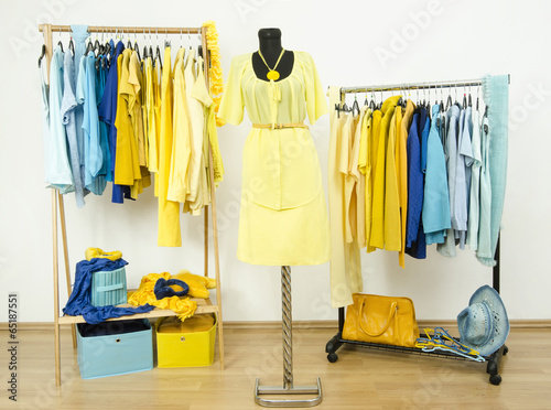 Wardrobe with yellow and blue clothes on hangers and mannequin.