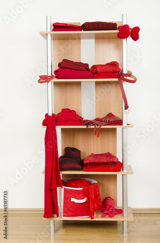 Tidy wardrobe with red clothes nicely arranged on a shelf.
