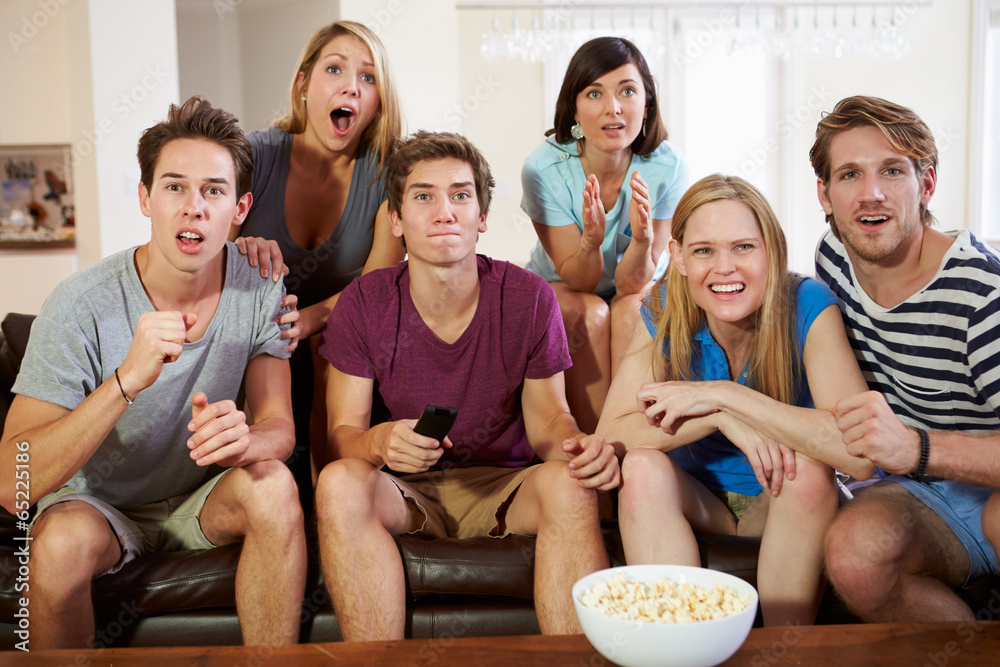 Obraz premium Group Of Friends Sitting On Sofa Watching TV Together