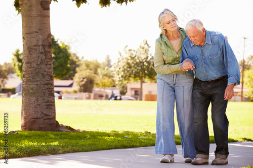 Senior Woman Helping Husband As They Walk In Park Together