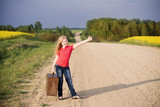 Smiling little girl holding a suitcase on a country road