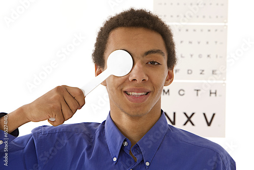 optometry -young man uses spoon occluder for test vision