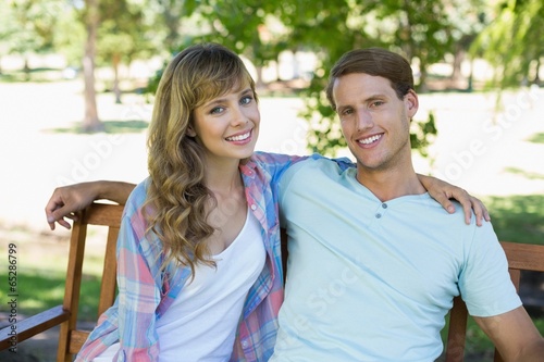 Cute couple sitting on bench in the park smiling at camera